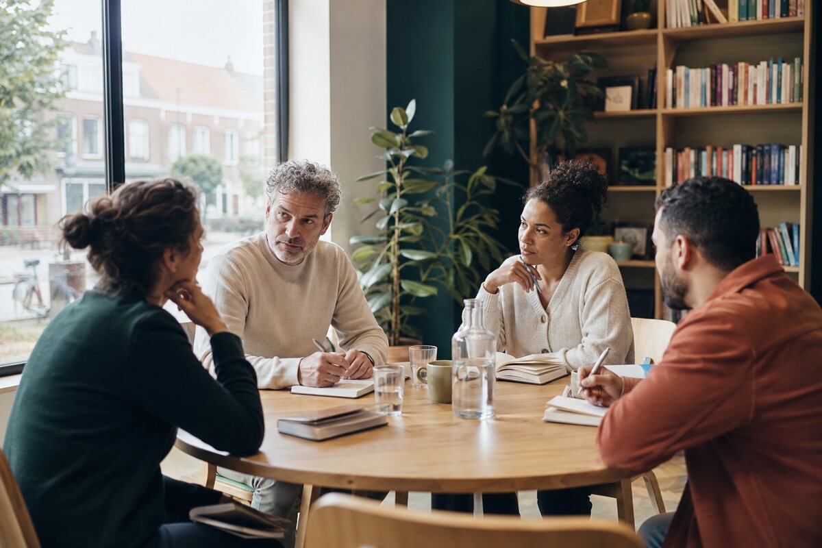 Vier mensen luisteren naar elkaar en leggen inzichten vast tijdens een gesprek aan een ronde tafel.