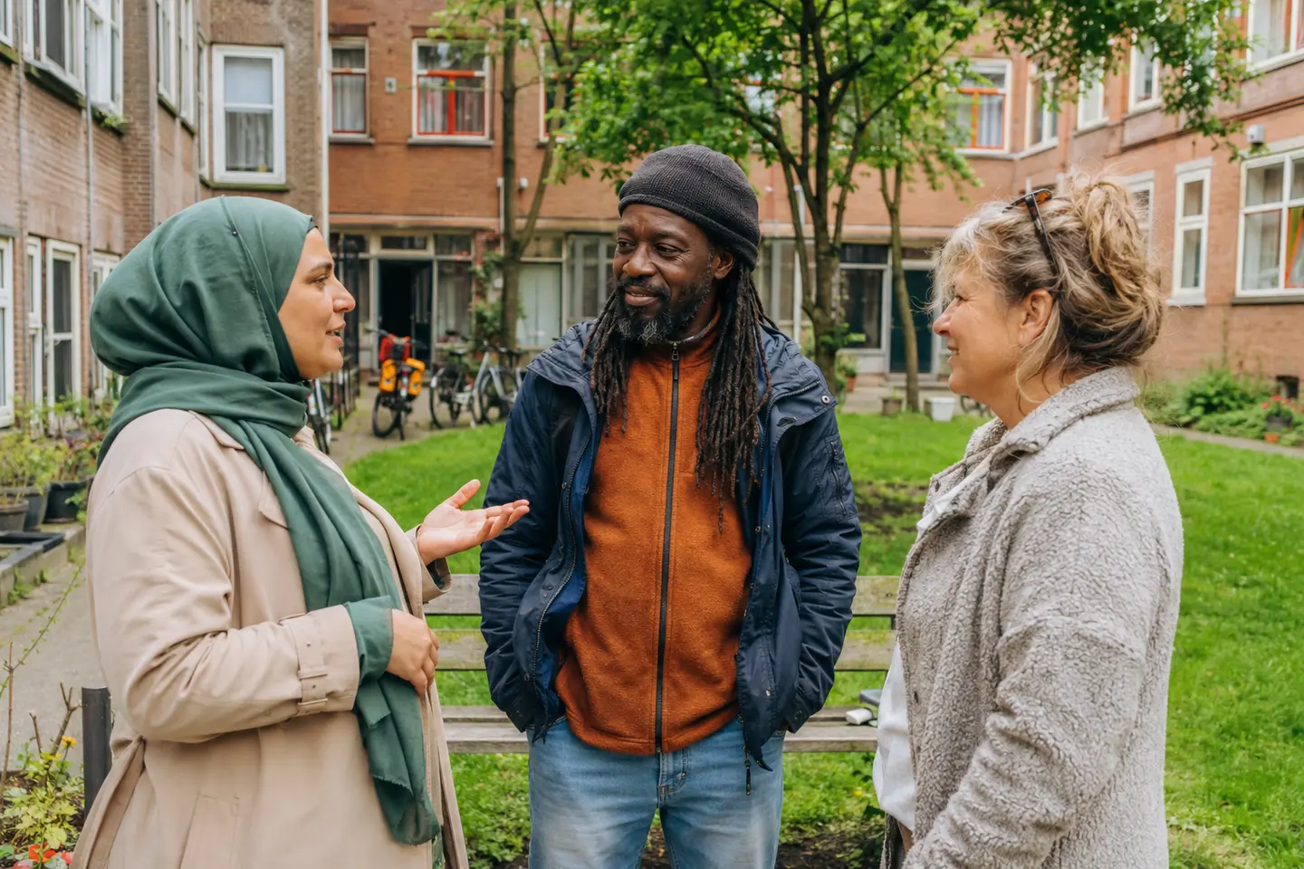 Drie buurtbewoners met verschillende achtergronden praten met elkaar in een gemeenschappelijke binnentuin.